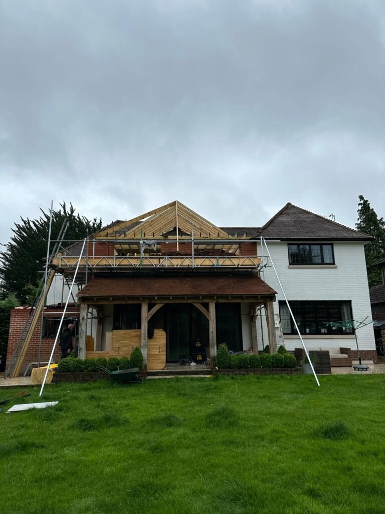 Rear house extension with oak-framed ground floor, scaffolding, and new timber gable roof structure under construction.