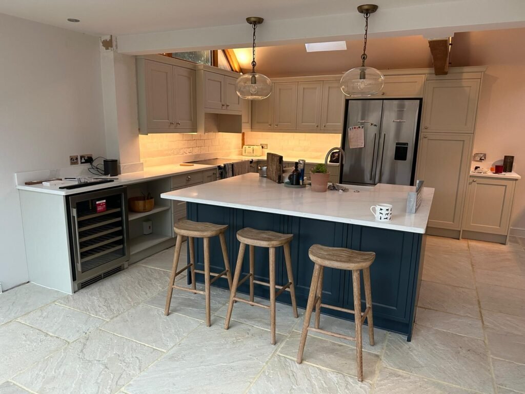 High-end kitchen with navy Shaker island, marble countertop, wooden bar stools, and globe pendant lights.