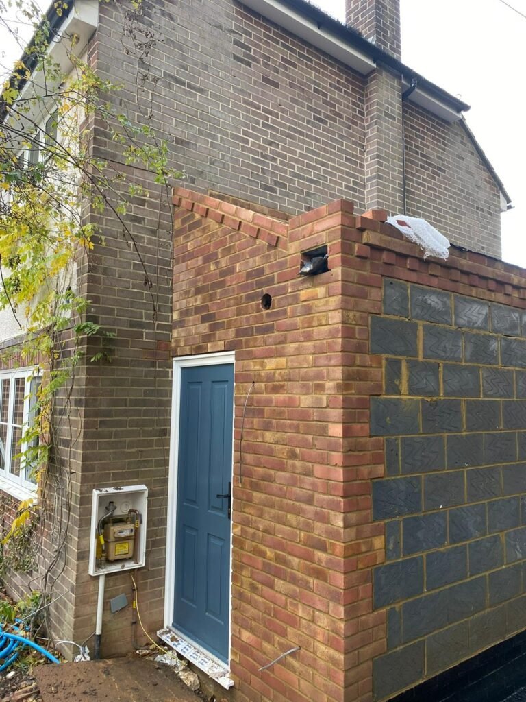 Small brick porch under construction with a blue panelled door installed against an existing brick house.