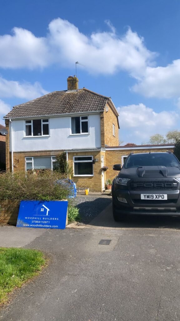 Woodhill Builders site sign in front of a two-storey house with a black Ford Ranger parked on the driveway.
