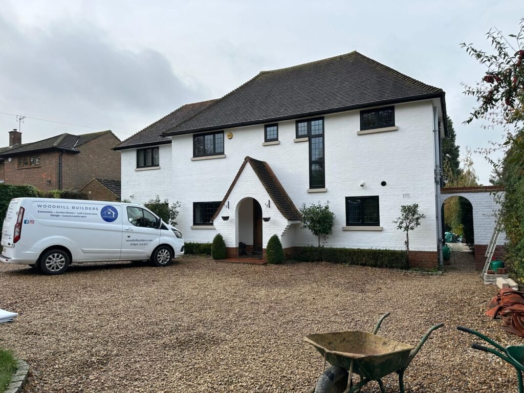 Renovated white brick house with black windows and a branded Woodhill Builders van on the gravel driveway